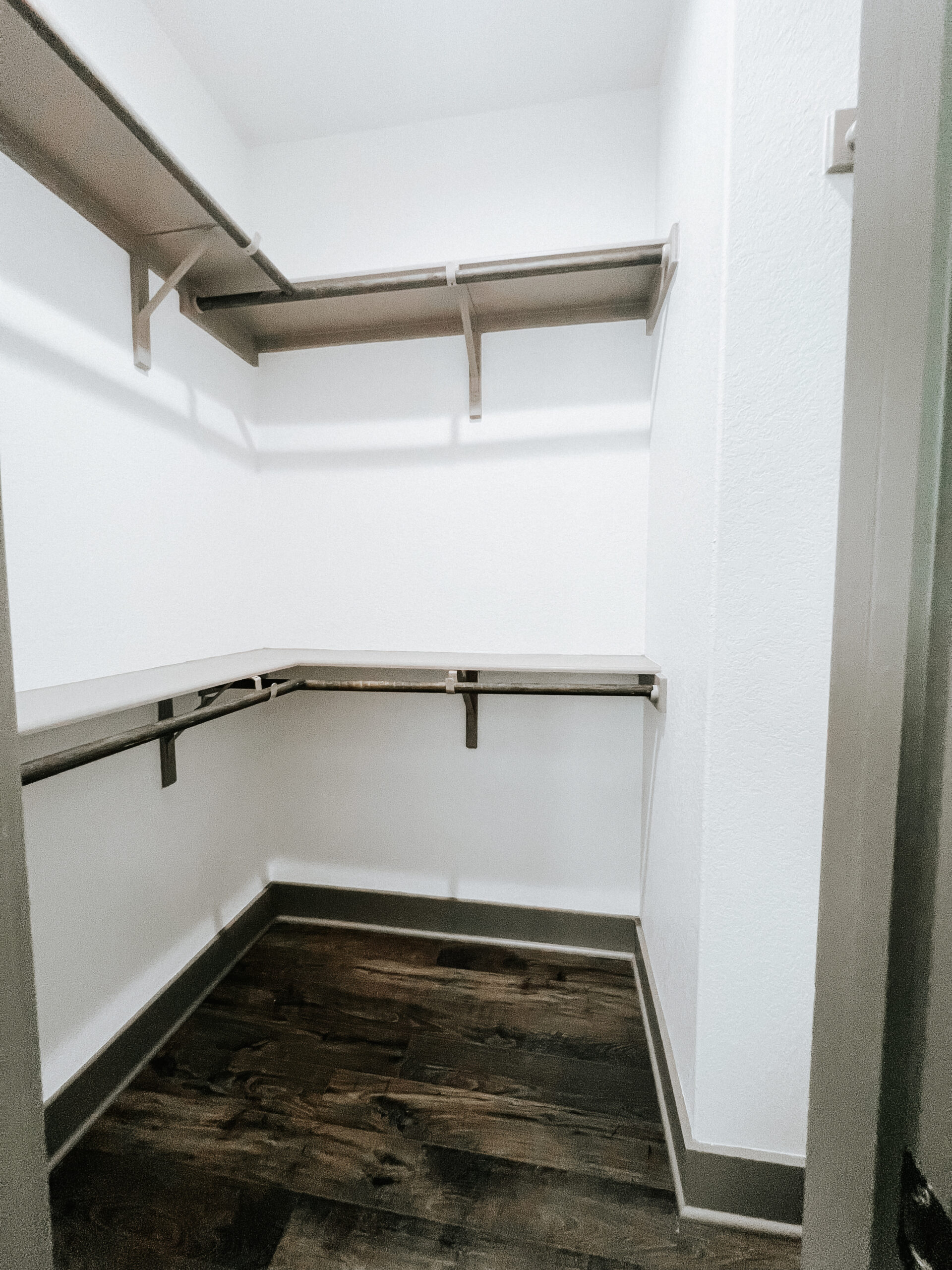 Empty walk-in closet with white walls, dark wood flooring, and metal shelving along two walls.